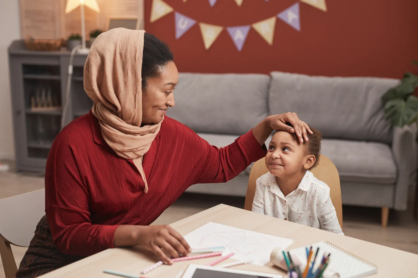 A mother smiles at her young daughter as they work through a lesson together at home