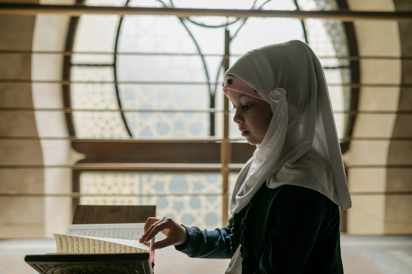 A girl reads the Qur’an beside a window